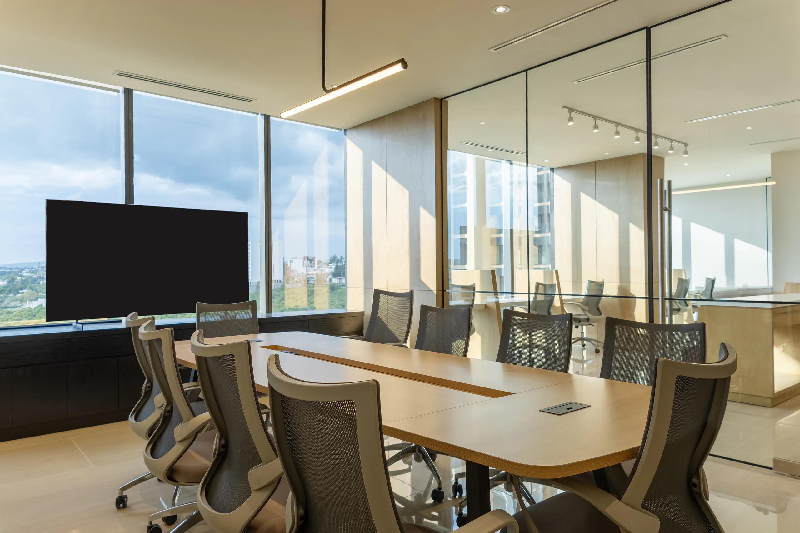 Sala de juntas con mesa larga, sillas ergonómicas y muros de cristal